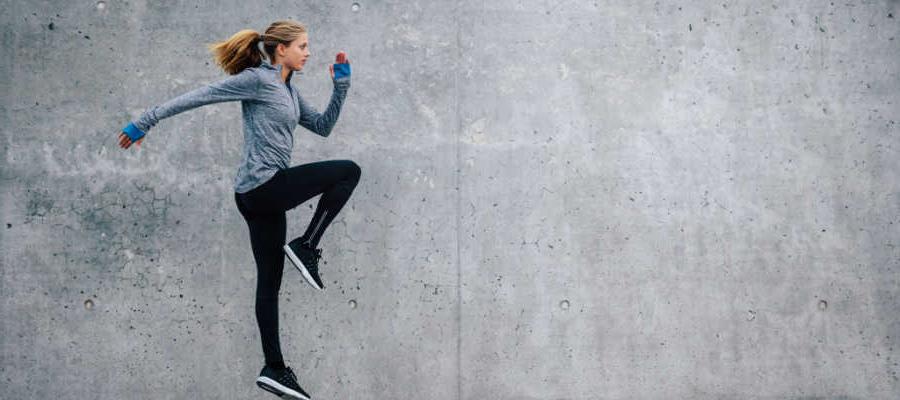 一位女跑步者在一堵灰色的墙旁边锻炼